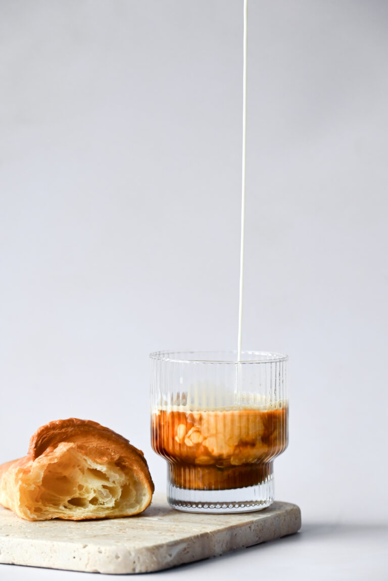 Kaffee Swirls durch von oben eingegeossene Milch und ein Croissant im Anbiss.