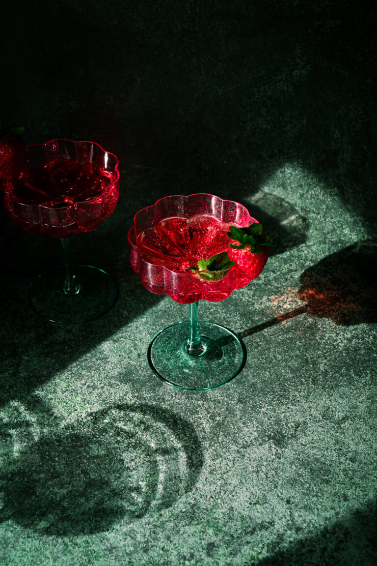 Roter Cocktail in tiefgrünem Setting mit Erdbeere