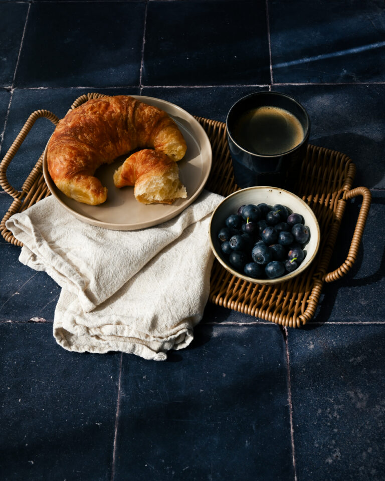 Croissant, Kaffee und Blaubeeren im Morgenlicht